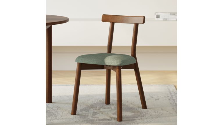 A mid-century style wooden dining chair with a green upholstered seat on a patterned rug.