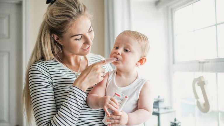 A woman using a gloved finger to brush or examine her baby's teeth