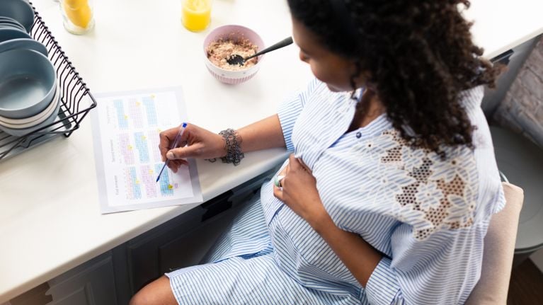 A pregnant woman writing on a pad at a kitchen island
