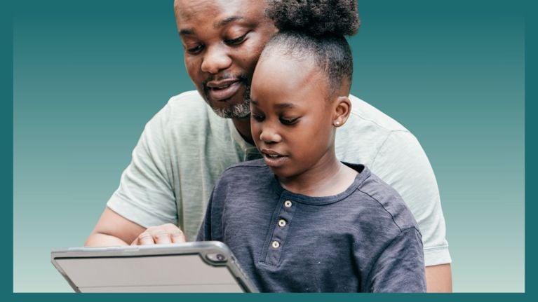 A father and daughter sit close together, smiling as they look at a tablet. The father gently points at the screen while the daughter focuses intently.