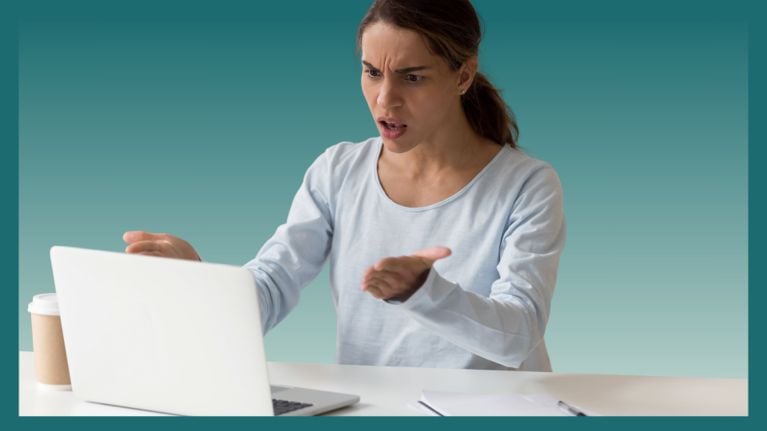 A frustrated woman gestures at her laptop with both hands, her face showing anger and confusion. A coffee cup and notebook sit on the desk beside her.