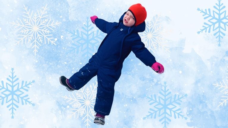 A toddler wearing a navy blue MEC Toaster Suit and red beanie lies in the snow making a snow angel. Pink mittens and snow-covered boots complete the outfit.