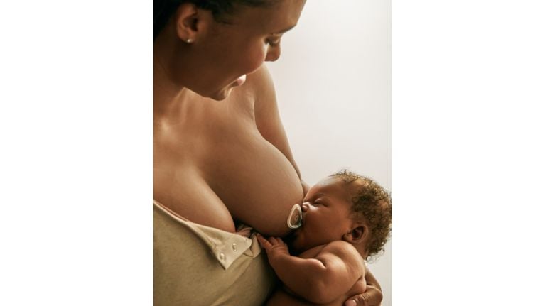 A mother breastfeeds her baby using a nipple shield. The baby is nestled in her arms and appears content while feeding.