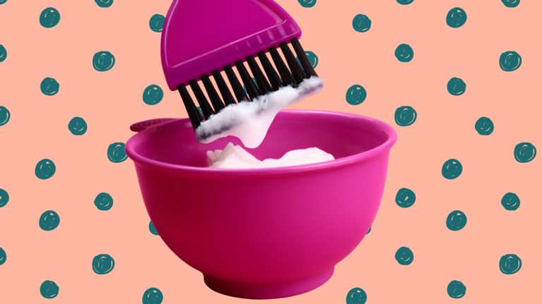 A close-up of a pink mixing bowl filled with white hair dye or conditioner. A matching pink dye brush with black bristles is dipped into the mixture. The background is peach-colored with teal polka dots, creating a playful, stylized look.