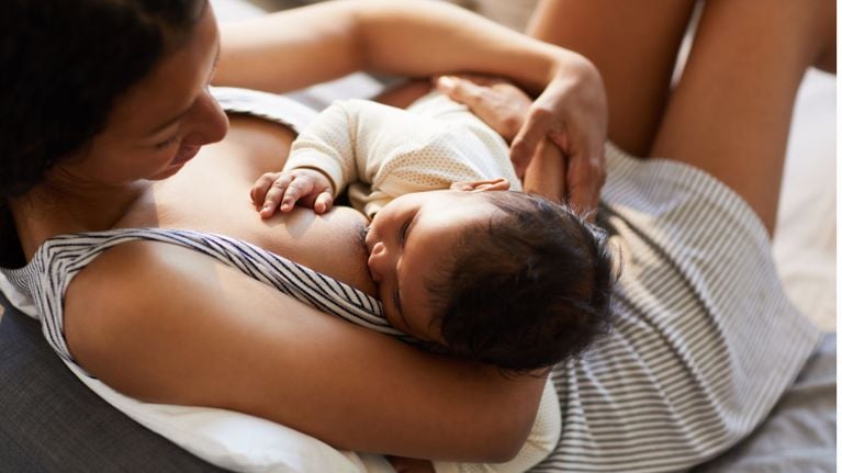 A mother comfortably breastfeeding her baby in bed, highlighting bonding and nourishment during the breastfeeding stage.