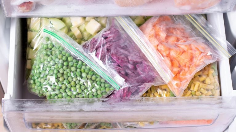A freezer drawer filled with clear zip-top bags of frozen food, including peas, diced zucchini, shredded beets, carrots, and pasta, neatly organized for easy meal prep.