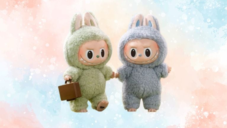 Two Labubu plush dolls in fluffy onesies—one mint green holding a brown suitcase and one grey—standing side by side, holding hands. The background is soft pastel watercolor.