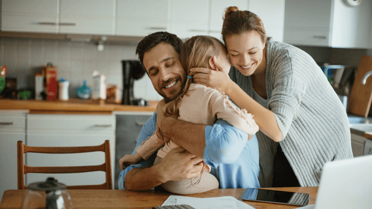 Two parents hold their young daughter near the kitchen table.