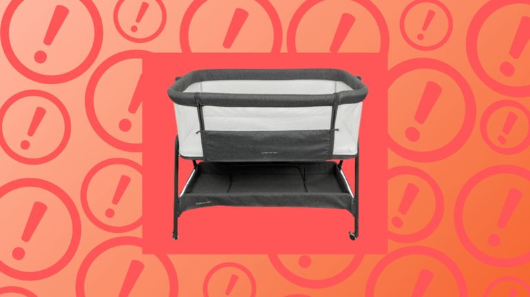 A grey bedside bassinet with mesh sides and a storage shelf underneath is shown centered against a bright coral background patterned with large exclamation mark icons, suggesting a warning or recall notice.