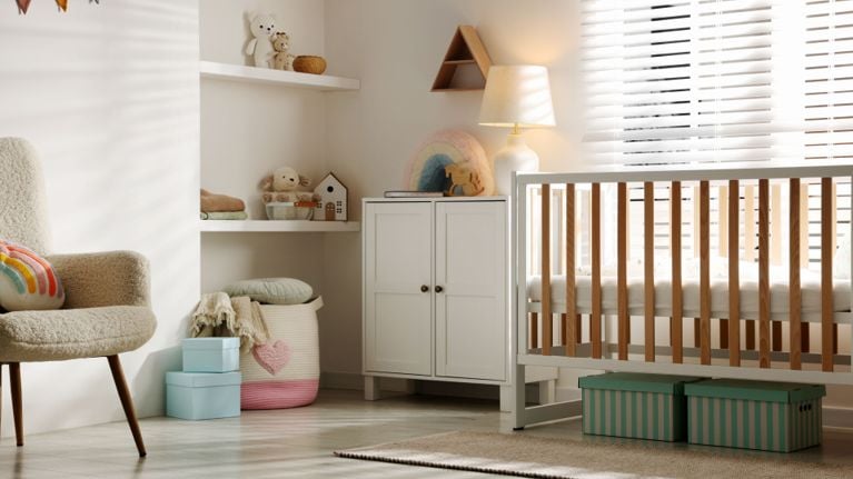 Calm nursery scene with a crib, armchair, storage baskets, soft toys, and warm lighting, creating a tidy, peaceful bedtime atmosphere.