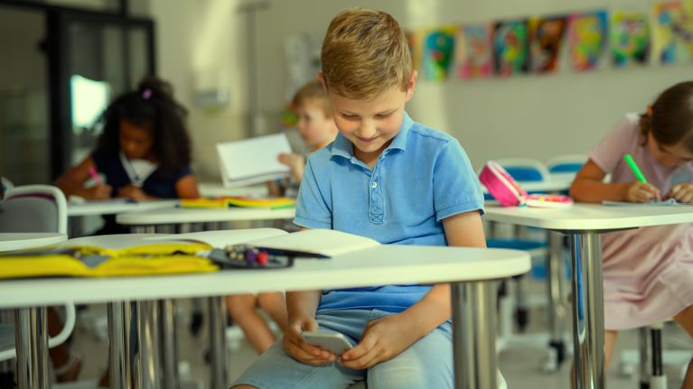 A boy in a classroom looking at a cell phone under his desk