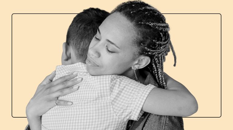 Black-and-white photo of a young child hugging an adult around the waist, the adult’s arms wrapped gently around the child, against a soft beige background.
