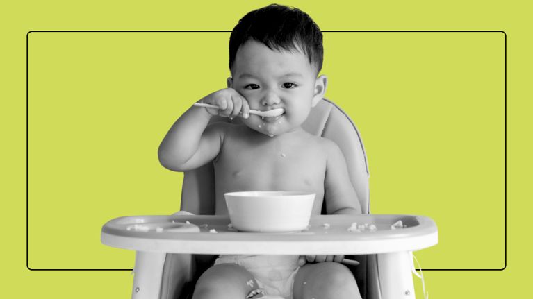 Close-up of a baby with mouth open, leaning toward a spoonful of food during feeding time.