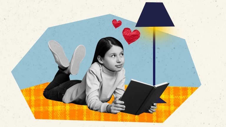 A grayscale tween girl lying on an orange rug, smiling and holding an open book under red paper hearts.