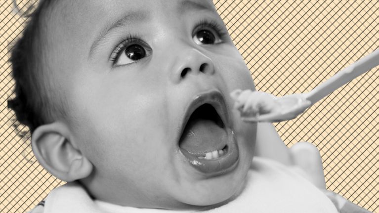 Close-up of a baby with mouth open, leaning toward a spoonful of food during feeding time.