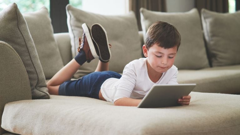 Young boy lying on a sofa using a tablet, demonstrating relaxed educational screen time.