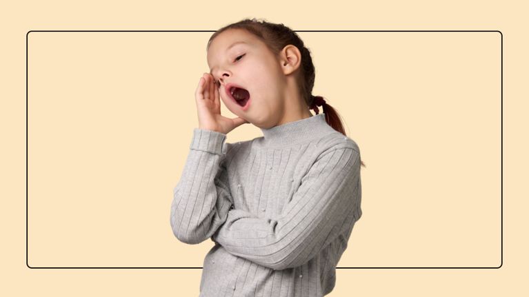 Child in a grey sweater yawning and rubbing their eye, shown against a beige background.