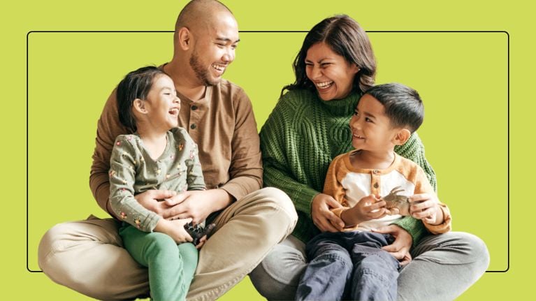 A father and mother sit on the floor laughing with their two young children against a lime green background.