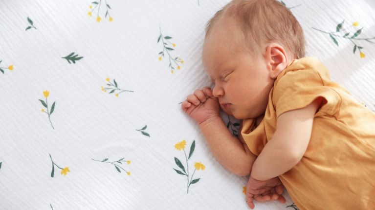 Newborn baby in a mustard yellow shirt sleeping on a white floral print crib sheet.