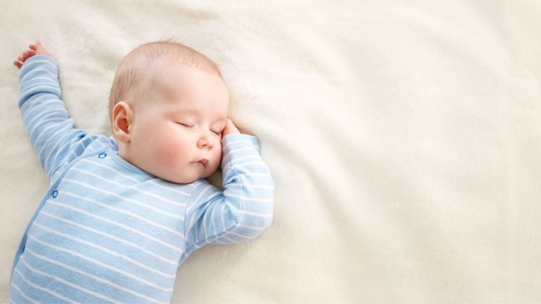 Baby in a blue striped onesie sleeping on a soft cream-colored plush blanket.