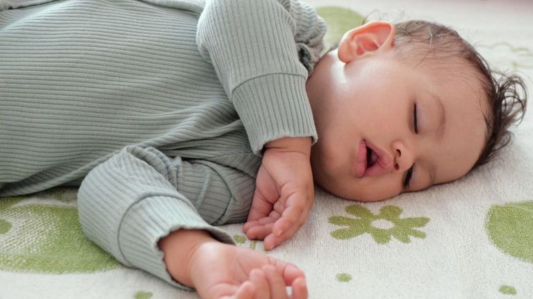 Infant with dark hair sleeping on a green floral crib sheet during a nap.