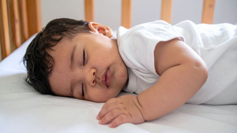 Baby sleeping on their stomach in a wooden crib with white bedding.