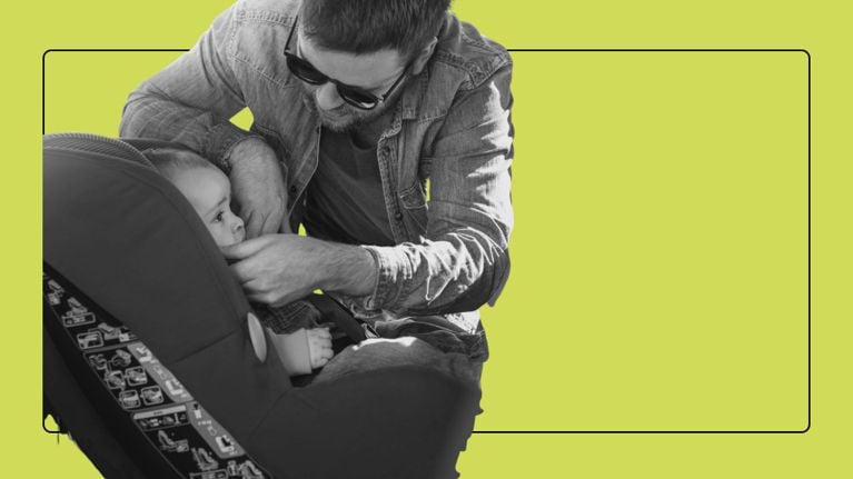 A father leans over to securely buckle his baby into a car seat.