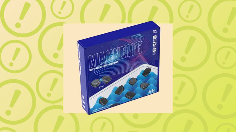 A blue retail box for a magnetic strategy game is displayed prominently. The box features the word "MAGNETIC" in bold letters and shows small, smooth black magnetic stones resting in a blue foam tray. The image is framed against a bright yellow backdrop repetitive with large exclamation point circles, signaling a high-priority safety recall or hazard alert for parents.