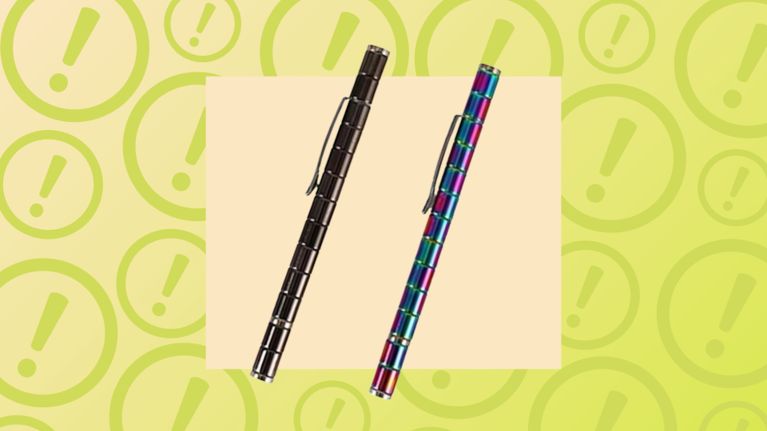 A product display features two long, segmented magnetic pens positioned diagonally. One pen is a sleek, dark chrome, while the other features a vibrant, multi-colored oil-slick finish. The background consists of a pale yellow square overlaid on a darker yellow pattern of large exclamation point warning symbols, suggesting a product recall or safety alert.
