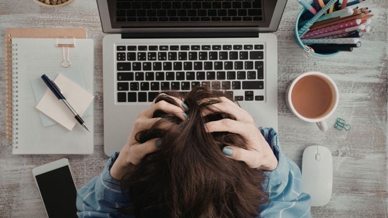 A stressed parent clutches their hair while sitting at a laptop, illustrating burnout and the mental load of parenting.