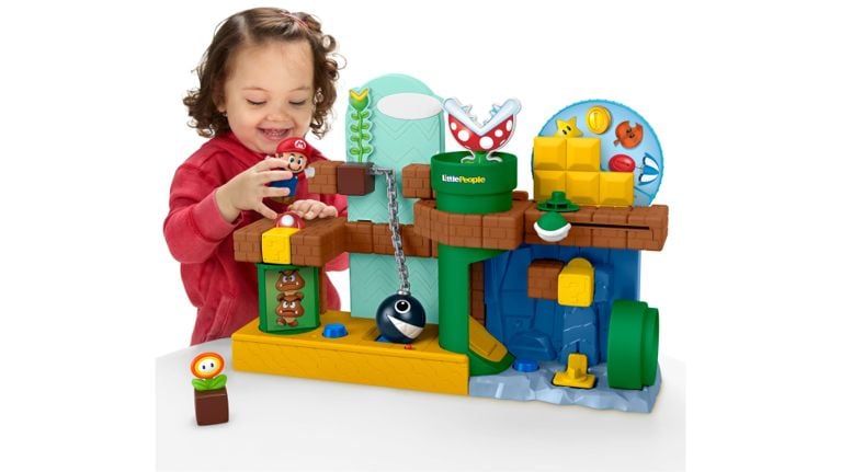 A smiling toddler plays with a Fisher-Price Little People Super Mario playset featuring Mario and classic game elements.