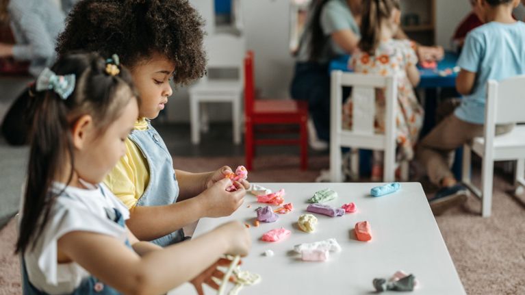 Three young children playing with a wooden Montessori object permanence box on a daycare rug.