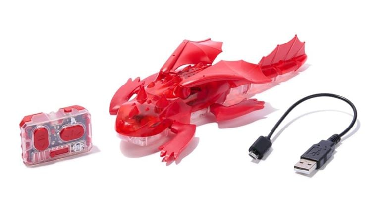 A translucent red remote-controlled Hexbots dragon with wings, a small remote, and a USB charging cable.