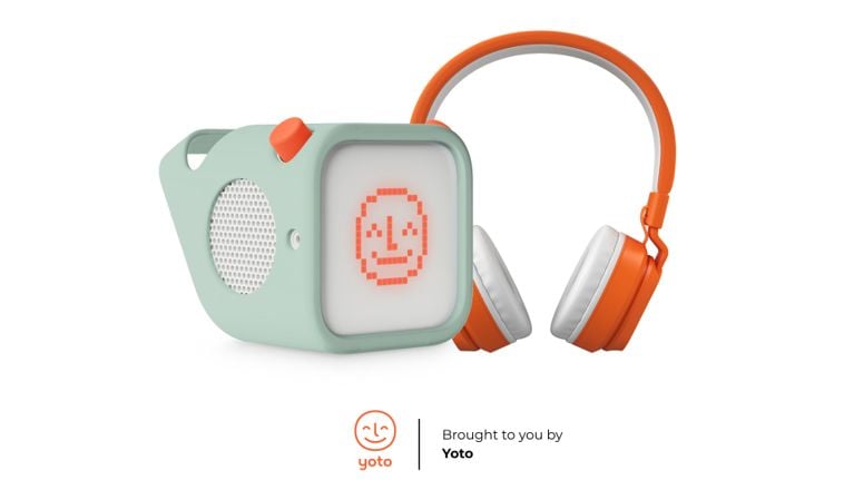Sage green Yoto Mini audio player with bright orange headphones and a pixel-art face on the front of the player.