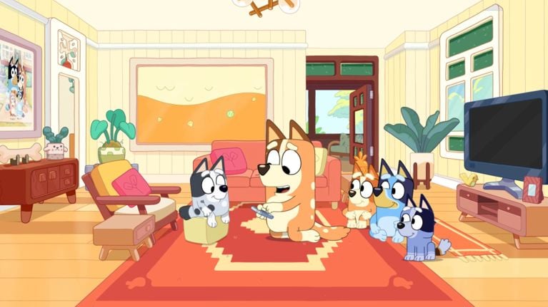 Five Bluey characters, including Bluey, Bingo, and Muffin, sitting on a red rug in a bright, animated living room.