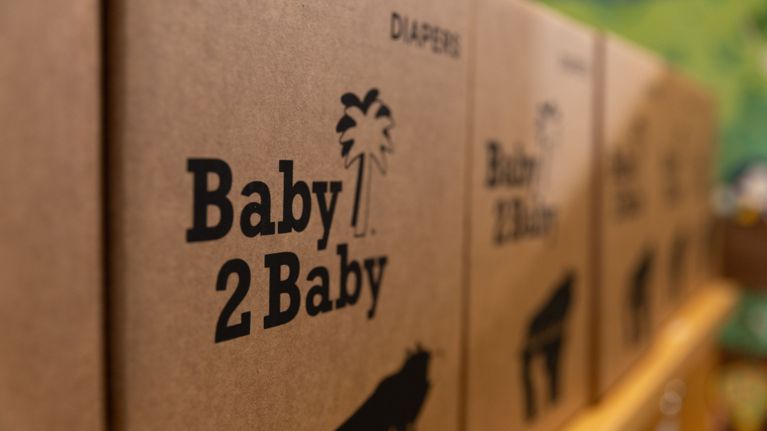 Close-up of brown cardboard boxes labeled Baby2Baby and Diapers, stacked in a row.