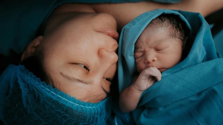 A mother in a hospital cap looking lovingly at her newborn baby wrapped in a blue blanket.
