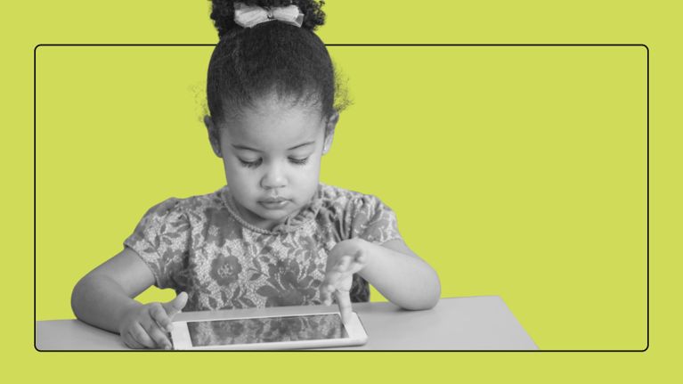 Young child with hair in a high bun focused on using a digital tablet at a desk.