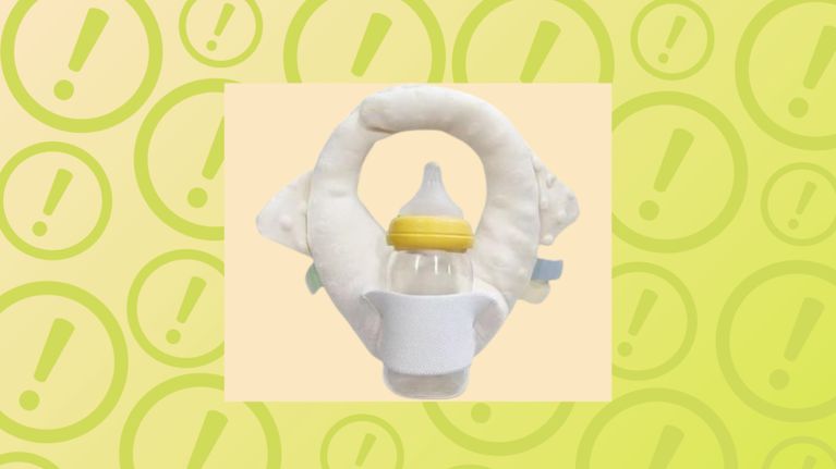 A white plush self-feeding baby bottle holder pillow on a yellow warning background for a product recall.