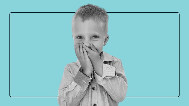 A young boy covers his mouth with both hands in a guilty, giggling gesture against a bright blue background.