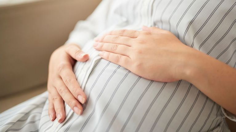 Close-up of a pregnant belly with both hands resting gently over a striped dress