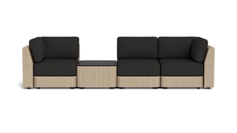 Studio product image of a modular wicker outdoor sofa with black cushions and a centre table against a black background.