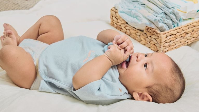 Baby lying on a blanket next to a basket of diapers