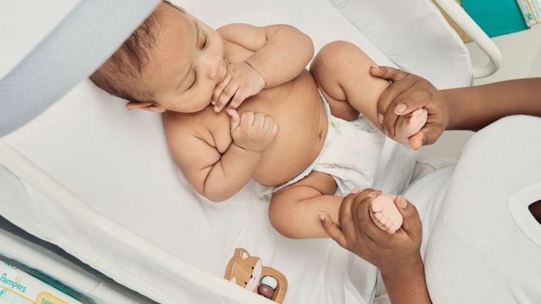 Baby lying on a blanket next to a basket of diapers