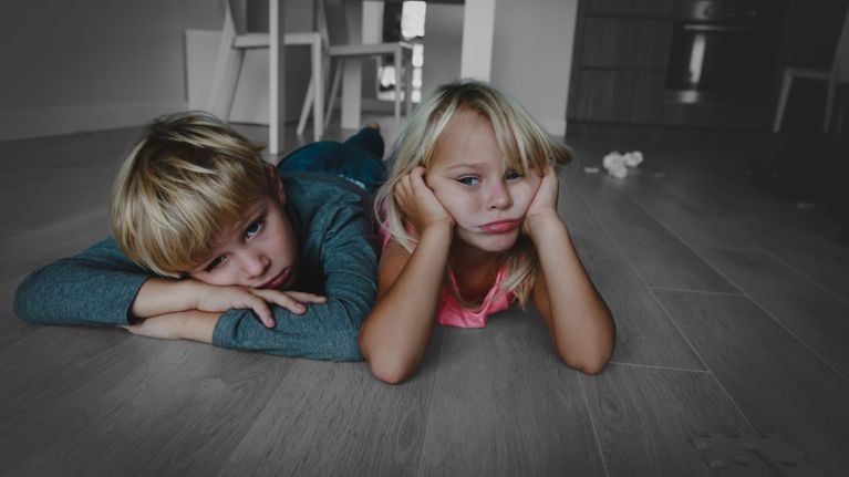wo young children lying on a hardwood floor with bored, unhappy expressions.