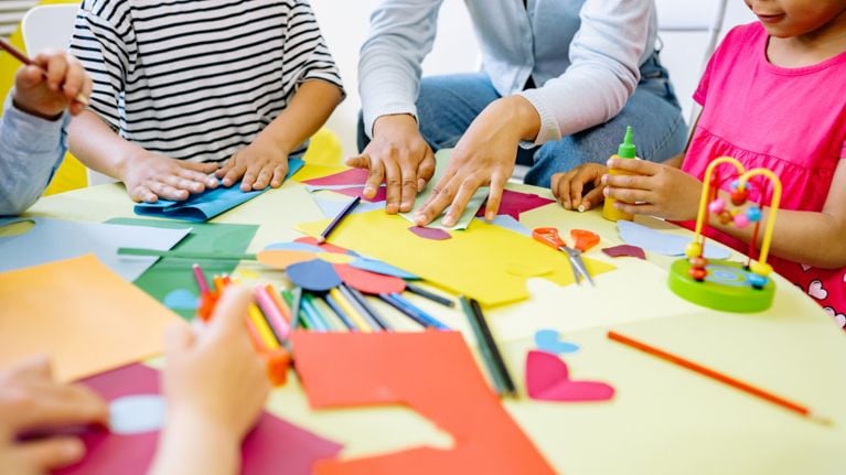 Children and an adult sit around a table doing crafts with colourful paper, markers, scissors and glue.