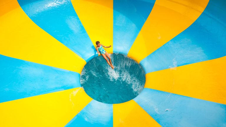 Child sliding into a bright blue-and-yellow bowl waterslide from an overhead view.