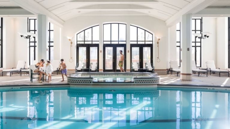 Bright indoor pool with lounge chairs and a family relaxing beside the water.