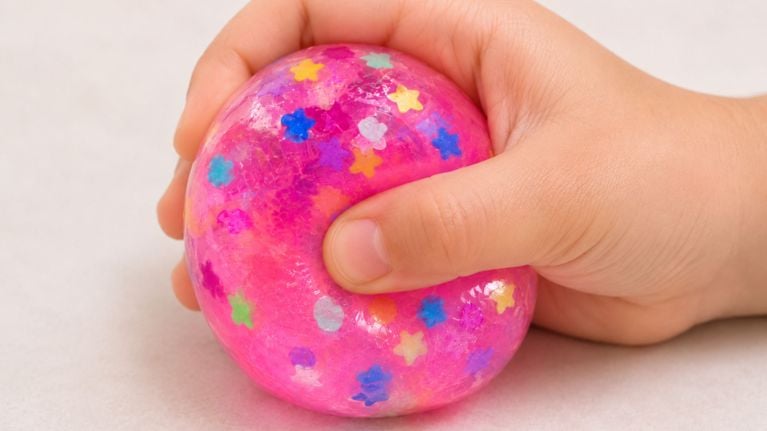 a child holds a pink squishy toy with colourful confettie inside.