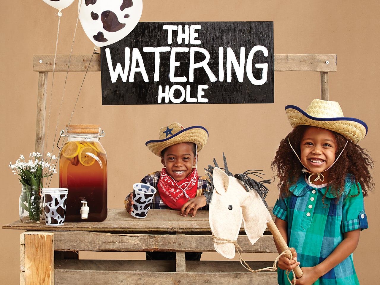 Two kids dressed as cowboys getting juice at a booth with a sign that says The Watering Hole